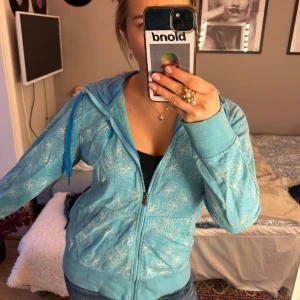 Blå huvtröja från Northrock Sports - Säljer en blå huvtröja från Northrock Sports med blommigt mönster. Tröjan har dragkedja och långa ärmar!