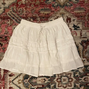 Vit volangkjol - Jättefin kjol med volanger/lager och broderidetaljer. Midjan kan justeras med banden som man knyter. Passar fint till midsommaren🪽