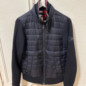 Svart jacka från Tommy Hilfiger - Säljer en stilren svart jacka från Tommy Hilfiger i ekologisk bomullsblandning. Jackan har en quiltad design med dragkedja framtill och långa ärmar. Perfekt för en snygg och bekväm look.