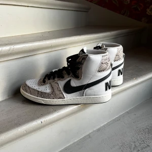Nike Sneakers Terminator High Cocoa Snake - Ovanliga och snygga Nike Terminator High Cocoa Snake sneakers vita. Skorna har hög modell med snörning och en tydlig Nike-logga på hälen. Perfekta för dig som vill sticka ut med stil. Ca 1100 kr nya.