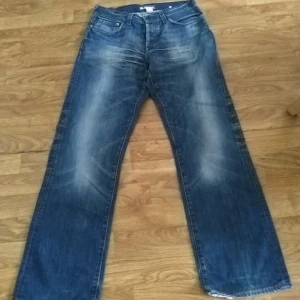 Blå jeansbyxor från HM - Säljer ett par blå jeansbyxor från HM med en klassisk femficksdesign och knappgylf. Byxorna har en avslappnad passform och är perfekta för en casual look. De har en lätt tvättad effekt för en trendig stil.