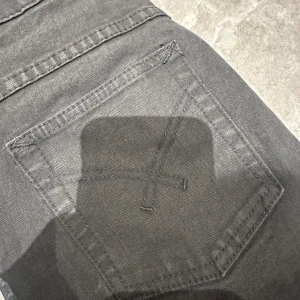Svarta jeans med detalj på bakfickorna  - Säljer dessa svarta jeans med detaljer på bakfickorna, jeansen är i övrigt väldigt fint skick men en hylsa har lossnat (lätt att laga), därav priset❤️