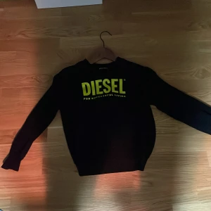 Svart tröja från Diesel - Säljer en svart tröja från Diesel med deras ikoniska logga i gult på bröstet. Tröjan har långa ärmar och en rund halsringning. Perfekt för en casual look.