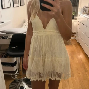 Vit ärmlös klänning - Säljer en söt vit ärmlös klänning med volangdetaljer och öppen rygg. Klänningen har en kort längd och knytband i ryggen för en justerbar passform. Perfekt för varma sommardagar!