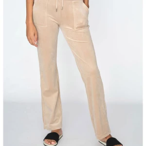 Beige mjukisbyxor med snörning - Snygga beige juicy byxor i ett mjukt material med snörning i midjan. Byxorna har en avslappnad passform och raka ben, perfekta för en bekväm stil. De har också praktiska fickor framtill.