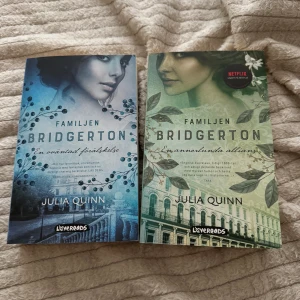 Familjen Bridgerton - En oväntad förälskelse och En annorlunda allians - Två böcker från serien Familjen Bridgerton av Julia Quinn. 'En oväntad förälskelse' har ett blått omslag med en kvinnas ansikte och 'En annorlunda allians' har ett grönt omslag med en annan kvinnas ansikte. Båda böckerna är utgivna av Lovereads och är del av en populär serie som även finns på Netflix.