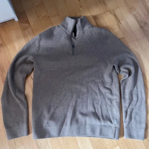 Beige tröja från Jack & Jones - Säljer en stilren beige tröja från Jack & Jones med dragkedja vid halsen. Tröjan är långärmad och tillverkad i ett mjukt material som passar perfekt för kyligare dagar. Perfekt för en avslappnad och snygg look.