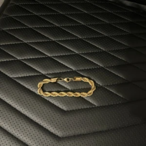 Guldigt tvinnat armband - Snyggt armband i guldig färg med tvinnad kedja och klassiskt lås. Perfekt accessoar för att lyfta din outfit med en stilren och trendig touch. Passar både till vardags och när du vill känna dig extra uppklädd.