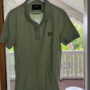 Ljusgrön pikétröja från Lyle & Scott - Snygg ljusgrön pikétröja från Lyle & Scott med klassisk krage och korta ärmar i storlek L men passar M. Tröjan har den ikoniska gula fågel-loggan broderad på bröstet och är gjord i mjuk bomull. Perfekt för en clean och stilren look.