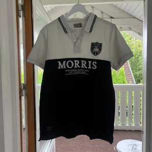 Vit och marinblå piké från Morris - Snygg pikétröja från Morris i storlek L men passar M. Tröjan är vit upptill och marinblå nedtill med tydlig logga och broderad badge på bröstet. Klassisk krage med två knappar och svarta ränder på kragen. Perfekt för en sportig och stilren look.