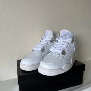 Nike Air Jordan 4 Retro White Chrome - Nike Air Jordan 4 Retro i helvitt skinn med silvriga detaljer och meshpaneler. Klassisk siluett med snörning, rund tå och Jumpman-logga i krom på hälen. Snygg och clean sneaker som sticker ut med sina metalliska accenter och robusta sula.