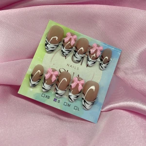 Zebra (S);Medium Almond - Snygga gelé press-on naglar i mandelform med nude bas, svartvita zebramönstrade tippar och 3D rosa rosetter. Perfekt för dig som vill ha en trendig och lekfull look. Kommer i storlek S: 15 mm, 11,5 mm, 12 mm, 11 mm, 9 mm 