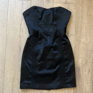 Svart axelbandslös kortklänning Guess - Snygg svart axelbandslös kortklänning från Guess med markerade sömmar och coolt leopardmönstrat foder. Klänningen har figurnära passform och dragkedja bak. En perfekt unik cocktail klänning!