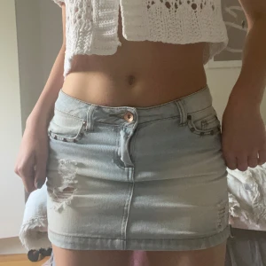 Ljusblå jeanskjol med slitningar - Snygg ljusblå jeanskjol i kort modell med detaljer framtill och på bakfickor.