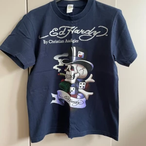 Mörkblå  t-shirt med tryck - Snygg mörkblå t-shirt  med stort färgglatt tryck av dödskalle, spelkort och tärningar på framsidan. Klassisk passform och korta ärmar. Ikonisk logga både fram och bak. Perfekt för dig som gillar streetwear och unika motiv.