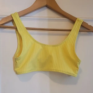 Topp och underdel - Gul bikini i sportig modell med ribbad struktur. Toppen har breda axelband och smidig knäppning bak, medan bikinitrosan har klassisk passform. Materialet är stretchigt och bekvämt. Storlek 158-164 I barnstorlek.  