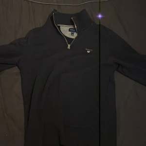 Mörkblå half zip tröja från Gant - Svart långärmad tröja från Gant med half zip och hög krage. Klassisk broderad Gant-logga på bröstet. Perfekt för dig som gillar stilrena och tidlösa plagg. Skön passform och enkel att matcha med det mesta.