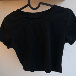 Svart croppad ribbad topp - En basic svart croppad fin topp som är ribbad  och korta ärmar. Enkel basic design med rund halsringning och skönt material.