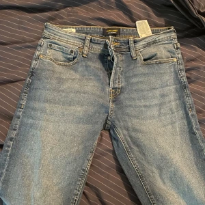 Blå tapered jeans från Jack & Jones - Snygga blå jeans från Jack & Jones i modellen Tapered/Mike. Klassisk femficksdesign, gul kontrastsöm och normal passform med avsmalnande ben. Tillverkade i slitstarkt denimtyg som ger en cool och avslappnad look.