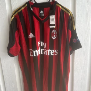 AC Milan Kaka' 22 Adidas matchtröja - AC Milan fotbollströja med Kaka' 22 på ryggen. Klassisk röd och svart randig design, guldiga detaljer på axlarna och officiella klubbmärken. Adidas-logga och Fly Emirates-tryck på bröstet. Kortärmad och tillverkad i lätt funktionsmaterial.