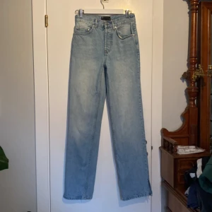  Jeans! -  Säljer ett par ljusblå jeans med klassisk femficksmodell och raka ben. Jeansen har hög midja och är tillverkade i 100% bomull för en äkta denimkänsla. Det är knappar ej dragkedja. Perfekta för en chill och stilren look. Slitsnedtill.  Innerbenslängd 81