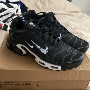 Nike Air Max Plus Tn Sneakers - Svarta Nike Air Max Plus sneakers med vita detaljer och tydlig TN-logga på hälen. Skorna har en vågig design på ovandelen, vit sula med synliga Air Max-enheter och klassisk snörning. Perfekta för dig som gillar streetwear och sportig stil.