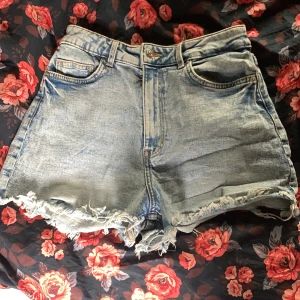 Högmidjade jeansshorts  - Snygga ljusblå jeansshorts från H&M Divided med hög midja och fransiga kanter. Klassisk femficksmodell med dragkedja och knapp framtill. Perfekta för sommaren och ger en avslappnad vibe till din outfit.