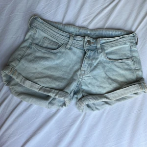 Ljusblåa jeansshorts  - Ljusblåa denimshorts med låg midja och klassisk femficksdesign. Shortsen har uppvikta benslut och bälteshällor, perfekta för sommardagar. Tillverkade i bomull för en skön och avslappnad känsla.