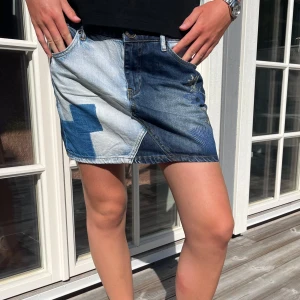 Patchwork jeanskjol i blå toner - Snygg kort jeanskjol med patchwork-design i olika blå nyanser. Kjolen har klassiska fickor fram och bak, bälteshällor och coola detaljer som kontrasterande sömmar och mönstrade partier. Perfekt för dig som gillar en unik och trendig stil.