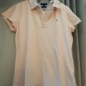 Ljusrosa pikétopp Tommy Hilfiger - Ljusrosa pikétopp från Tommy Hilfiger i slim fit-modell. Klassisk krage, korta ärmar och knappar framtill. Liten broderad logga på bröstet. L i storlek men skulle säga M