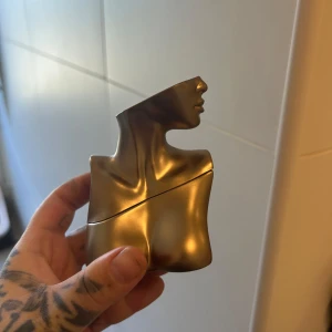 Eilish parfym av Billie Eilish 30ml - Unik parfymflaska i form av en bronsfärgad byst, designad av Billie Eilish. Flaskan har en cool metallisk finish och skulptural form som sticker ut i samlingen. Perfekt för dig som gillar snygg design och vill ha något annorlunda på hyllan. Helt ny, oanvänd 