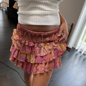 Färgglad volangkjol med paisleymönster - Supersöt kort volangkjol i rosa, gult och rött med paisleyinspirerat mönster. Kjolen har bred smock i midjan och flera lager volanger som ger en flowy look. Perfekt för sommaren!