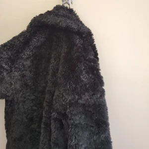 Svart fluffig pälsjacka - Mysig svart pälsjacka med oversized känsla och stora krage. Jackan är superfluffig och perfekt för kalla dagar när du vill sticka ut och hålla dig varm. Passar dig som gillar statement-plagg och vill ha en riktigt skön jacka med mycket volym.