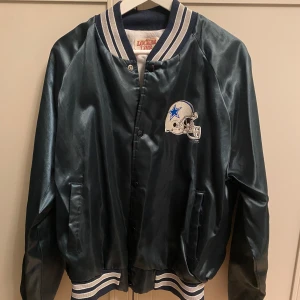 Vintage / Retro - Jacka - Cowboys bomberjacka - Locker Line - Vintagejacka från Locker Line med Dallas Cowboys-tryck och hjälm på både fram- och baksida. Bra skick för att ha så många år på nacken. Muddarna och kragen är fina och inte noppriga. 