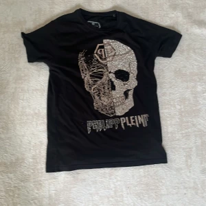 Svart Philipp Plein t-shirt med döskalle - Svart t-shirt från Philipp Plein med korta ärmar och en stor glittrig döskalle framtill. Snyggt tryck med silverdetaljer och logga. Skön passform och cool design som sticker ut. Perfekt för dig som gillar statement-plagg.