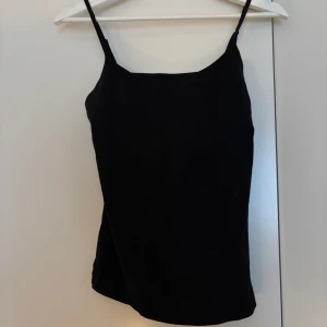 Svart linnetopp från Basic You - En svart, enkel och stilren linnetopp från Basic You i ekologisk bomull. Toppen har smala axelband och rak passform, perfekt att matcha med jeans eller kjol. Snygg och basic för en clean look.