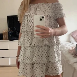 Vit prickig offshoulder volangklänning! - Supersöt kort volangklänning i vitt med svarta prickar. Offshoulder-modell med flera lager volanger som ger en luftig och lekfull känsla. Perfekt för varma dagar och somriga vibes.