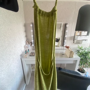 Grön stickad sommar klänning med knyt i nacken - Snygg grön sommar klänning i stickat material med smala axelband och knyt i nacken. Klänningen har en avslappnad passform och en cool, öppen rygg. Perfekt för varma dagar när du vill sticka ut lite extra.