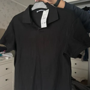 Svart ribbad pikétröja - Svart pikétröja från zara i ribbad bomull. Klassisk krage, korta ärmar och stilren look som passar perfekt till jeans. Enkel och snygg att matcha med olika outfits.