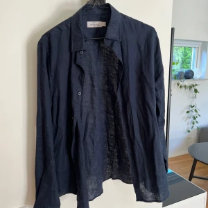 Mörkblå linneskjorta från Dressmann - Snygg mörkblå skjorta från Dressmann i premium linne. Skjortan har klassisk krage, knäppning framtill och långa ärmar. Perfekt för dig som gillar en luftig och stilren look under varmare dagar.