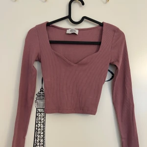 Rosa ribbad croppad topp från Chiquelle - Croppad långärmad topp i en snygg dammigt rosa nyans från Chiquelle i storlek XS. Toppen är ribbad och har en djup v-ringning framtill. 