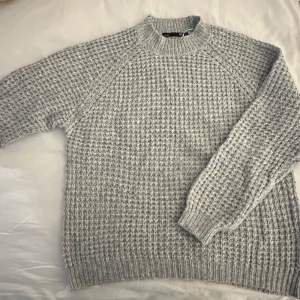 Grå stickad tröja  - Säljer en grå stickad tröja från Lager157 med grov struktur och rund hals. Tröjan har långa ärmar och ribbade muddar vid ärmslut och nederkant. I gott skick, använd få gånger.