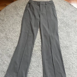 Grå kostymbyxor från Madlady - Snygga grå kostymbyxor från Madlady i klassisk modell med pressveck och raka ben. Byxorna har hällor för bälte, fickor bak och är midwaist. Perfekta för en clean och stilren look, passar till både sneakers och boots. Aldrig använda men prislappen är tyvärr inte kvar.
