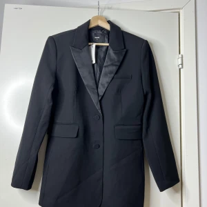 Svart kavajkostym från Bikbok  - Svart kavajkostym från Bikbok. Kavajen har snygga satindetaljer på slaget, två fickor med lock och knäppning framtill.