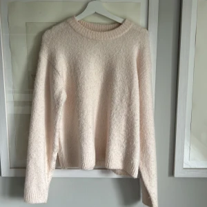 Ljusbeige stickad tröja från H&M - Supermjuk och fluffig ljusbeige stickad tröja från H&M. Tröjan har rund halsringning, ribbade muddar och lång ärm. Perfekt för lager-på-lager och chill dagar. Enkel och stilren design som är lätt att matcha.