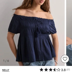 Mörkblå offshoulder blus från Nelly - Supersöt mörkblå blus från Nelly med offshoulder och korta puffärmar. Smockad överdel och lös passform nedtill, med knytband framtill för extra detalj. Perfekt till jeans eller kjol för en chill och trendig look.
