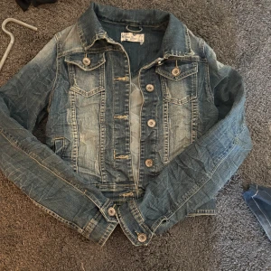 Blå jeansjacka från Blue Rags - Snygg och unik blå jeansjacka från Blue Rags med klassisk krage, bröstfickor med lock och knappar framtill. Jackan har slitna detaljer och kontrastsömmar som ger en cool vintagekänsla. Pris kan diskuteras vid snabb affär 