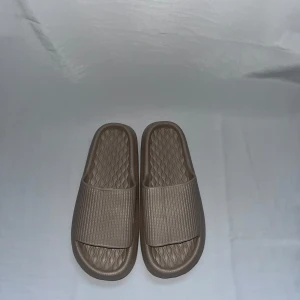 Beige slides sandaler i syntet - Snygga beige slides sandaler med ribbad ovandel och mönstrad sula för extra komfort. Tillverkade i mjukt syntetmaterial, perfekta för chill dagar eller att glida runt hemma. Enkel och stilren design med öppen tå och platt sula.