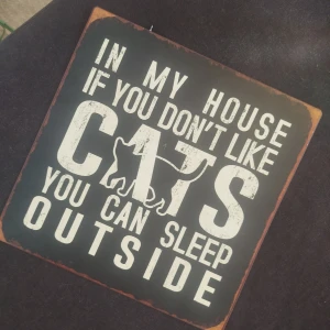 In My House If You Don't Like Cats You Can Sleep Outside - En humoristisk skylt med texten 'In my house if you don't like cats you can sleep outside' och en kattillustration. Perfekt för kattälskare som vill visa sin kärlek till katter på ett roligt sätt.