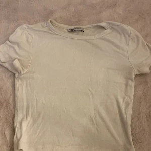 Vit basic t-shirt från Zara - Enkel vit t-shirt från Zara i mjuk bomull. Klassisk rund halsringning och korta ärmar, perfekt till jeans eller kjol. Snygg och stilren modell som är lätt att matcha med allt. Storlek S.